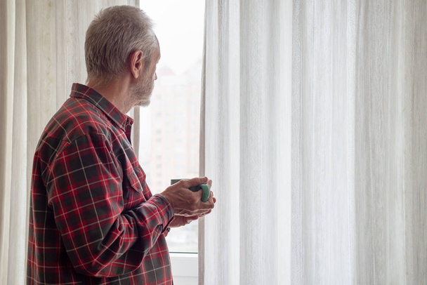 Homem maduro bebendo seu café em uma xícara verde, enquanto ele está olhando pela janela
 - Foto, Imagem
