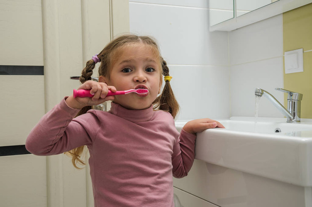 Girl child brushing her teeth with a toothbrush in the bathroom - Foto, immagini