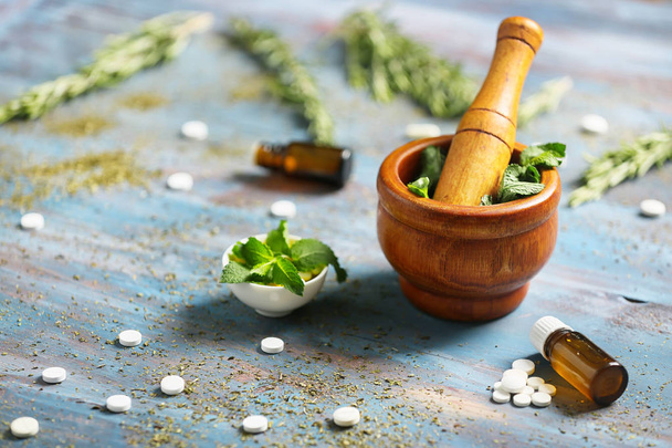 Mortar with fresh mint, essential oil and pills on color wooden table - Foto, Bild