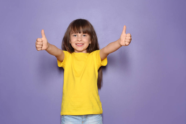 Little girl in t-shirt showing thumb-up gesture on color background - Foto, imagen