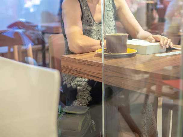 Aged woman wearing casual dress reading book and a cup of coffee on wooden table in cafe. - Foto, immagini