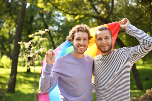 glückliches homosexuelles Paar mit Regenbogenfahne im Park - Foto, Bild