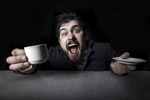 cheerfully crazy bearded man emotionally shouts into the camera with a cup of coffee in his hand - Photo, Image