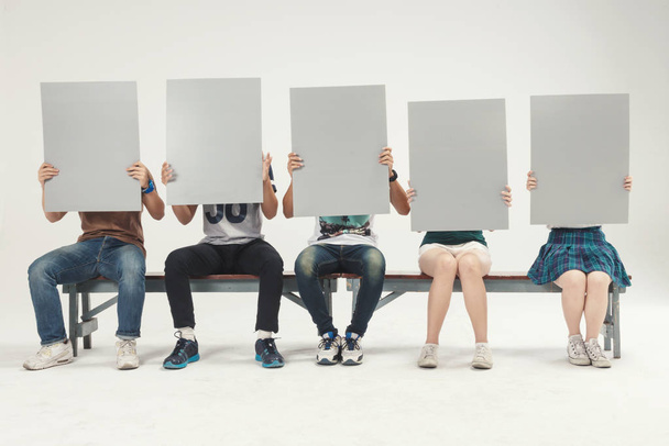 Grupo de jóvenes sentados sosteniendo, letrero en blanco para añadir carácter aislado sobre fondo blanco
  - Foto, Imagen