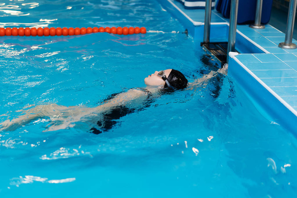 Zwemles voor kinderen in het zwembad - mooi fair-gevild meisje zwemt in het water - Foto, afbeelding