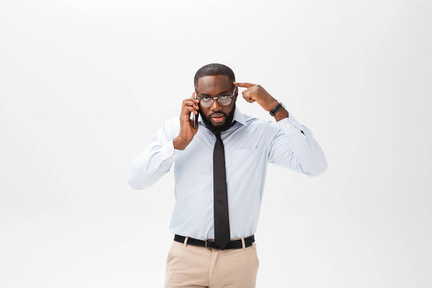 Πορτρέτο του μια συγκεχυμένη νεαρός αφρικανική ντυμένος με άσπρο πουκάμισο μιλάει στο κινητό τηλέφωνο και χειρονομώ απομονωθεί σε λευκό φόντο - Φωτογραφία, εικόνα