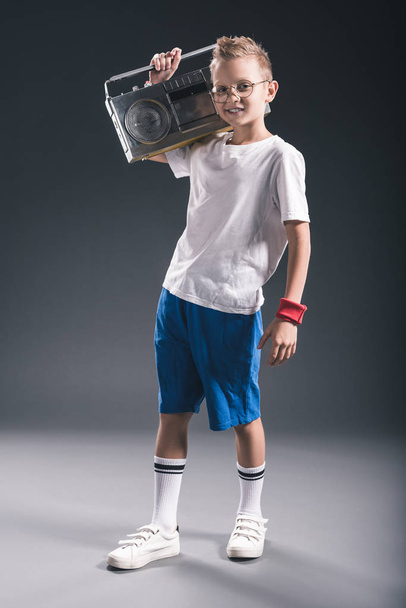 stylish preteen boy holding boombox on shoulder on grey backdrop - Fotoğraf, Görsel