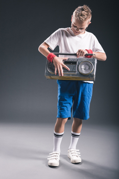 stylish preteen boy in eyeglasses holding boombox on grey backdrop - Φωτογραφία, εικόνα