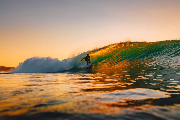 September 8, 2018. Bali, Indonesia. Surfer ride on barrel wave at warm sunset. Professional surfing in ocean, Bingin beach - Photo, Image