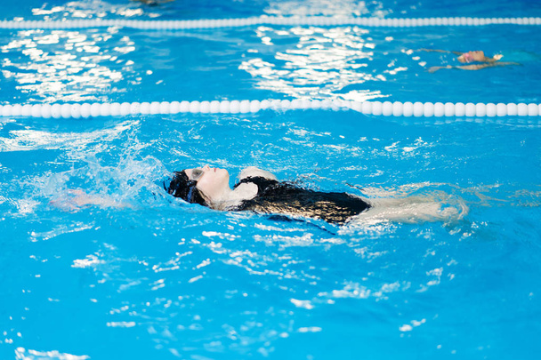 μαθήματα κολύμβησης για παιδιά στην πισίνα - όμορφη κοπέλα με ανοιχτόχρωμο δέρμα που κολυμπά στο νερό - Φωτογραφία, εικόνα