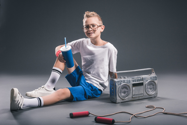 boy in eyeglasses with soda drink, boombox and jump rope on grey backdrop - Φωτογραφία, εικόνα