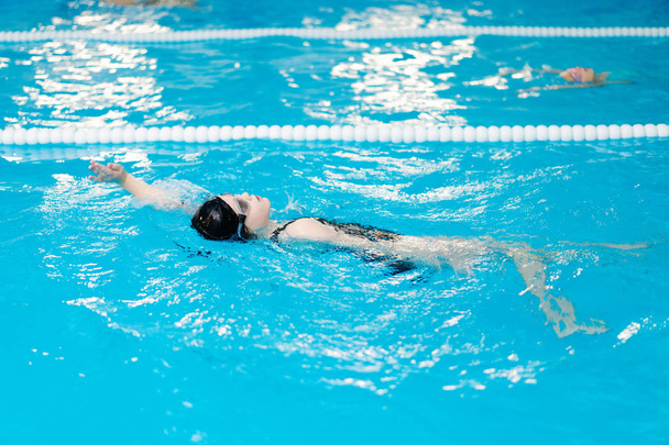 μαθήματα κολύμβησης για παιδιά στην πισίνα - όμορφη κοπέλα με ανοιχτόχρωμο δέρμα που κολυμπά στο νερό - Φωτογραφία, εικόνα