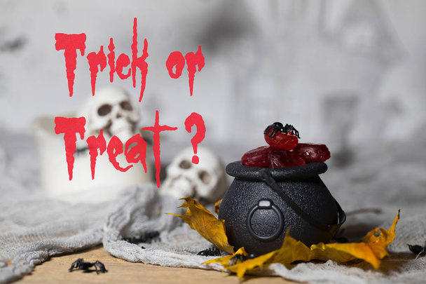 Trick or treat! Candles in the cauldron for Halloween. Skulls in the background - Photo, Image