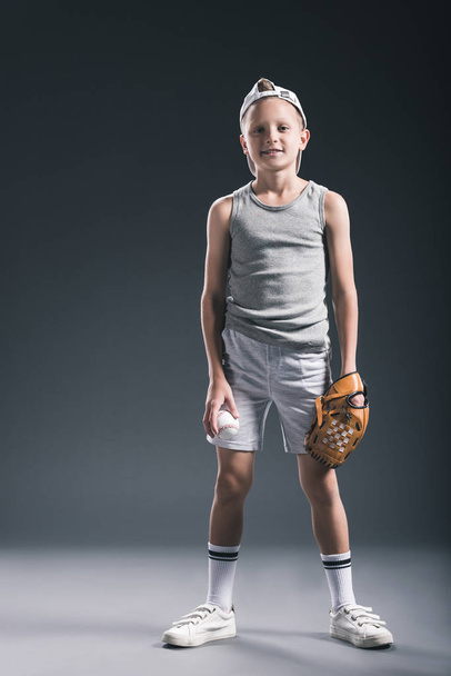 niño preadolescente en gorra con guante de béisbol y pelota sobre fondo gris
 - Foto, Imagen