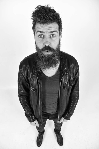 Man with beard and mustache on surprised face looking at camera. Macho wears leather jacket, white background. Menswear and fashion concept. Hipster looks surprised while posing in stylish outfit - Foto, Imagem