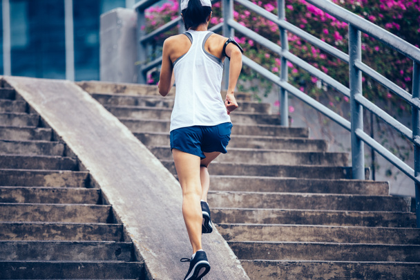 Young woman runner sportswoman running up city stairs - 写真・画像