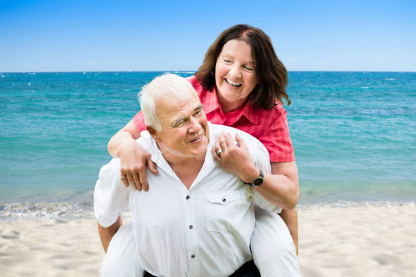 Retrato de un hombre mayor feliz dando Piggyback a su esposa en la playa
 - Foto, imagen