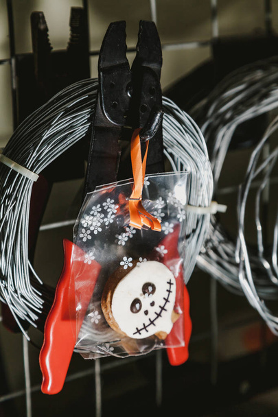 Halloween in the workshop. Halloween cookies weigh on a background of a round skein of wire and pliers with red handle - Fotografie, Obrázek