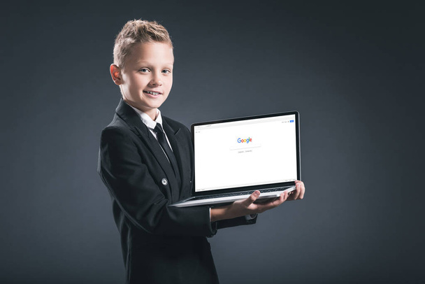 smiling boy in businessman suit showing laptop with google website on screen on grey background - Fotoğraf, Görsel