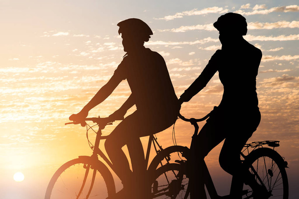 Silhouette eines Paares, das bei Sonnenuntergang Fahrrad fährt - Foto, Bild