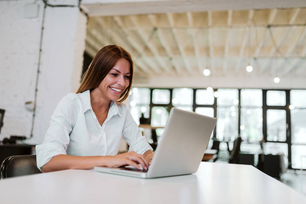 Beautiful woman with a toothy smile working on a laptop in modern office. - Zdjęcie, obraz