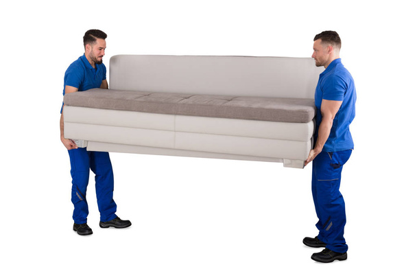 Two Young Male Movers Carrying Sofa On White Background - Foto, immagini