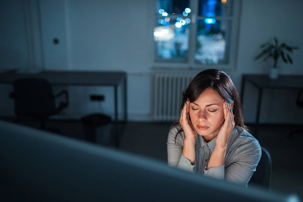 Tired and exhausted young woman sitting in front of computer screen at night. - Фото, зображення