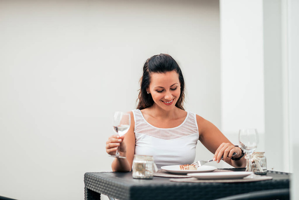 Smiling young woman drinking a glass of wine and having a piece of cake. - Φωτογραφία, εικόνα