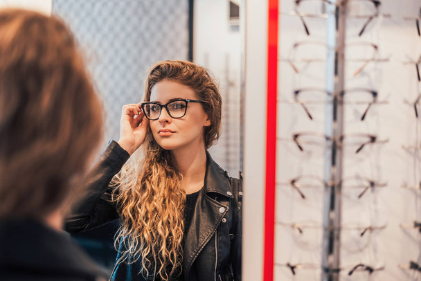 Woman trying new glasses, looking on mirror. - Foto, Bild