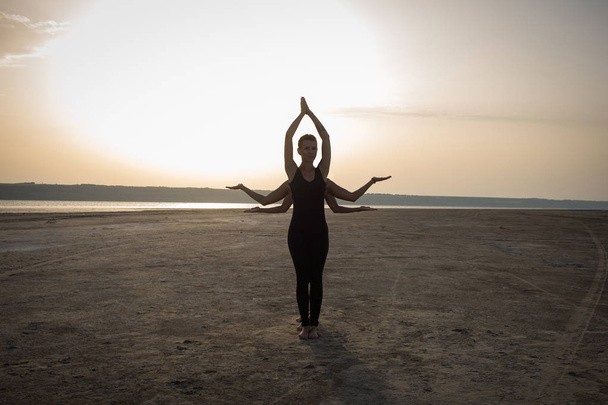 young women practicing yoga poses and asanas. Partner yoga, acrobatic yoga. Yoga class in black wear training in desert during sunset - Photo, Image