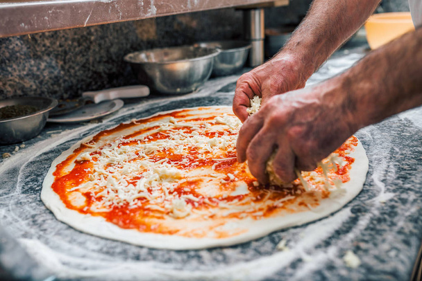 Chef spreading cheese on pizza base. Close-up. - Fotó, kép