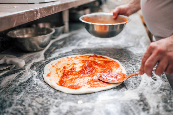 Image en gros plan du chef préparant la base de pizza à la sauce tomate
. - Photo, image