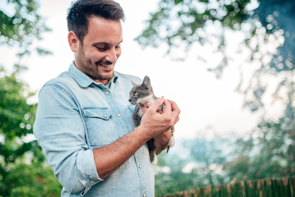 Handsome man is holding and hugging cute cat outdoors. - Zdjęcie, obraz