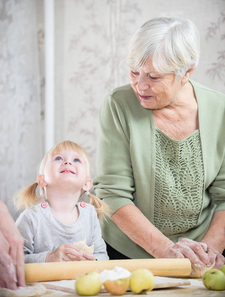 Una anciana haciendo pastelitos con una niña. La chica mirando hacia arriba
 - Foto, Imagen