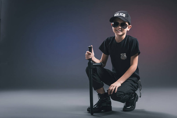 smiling boy in policeman uniform and sunglasses on dark background - Photo, Image
