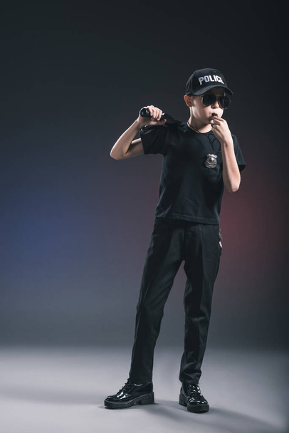 boy in policeman uniform and sunglasses with whistle on dark background - Photo, Image