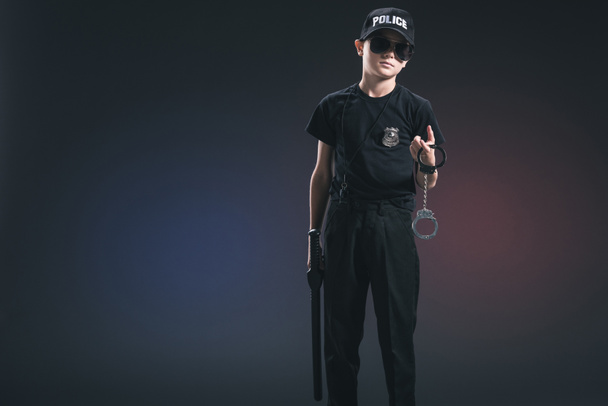 boy in policeman uniform and sunglasses with handcuffs on dark background - Photo, Image