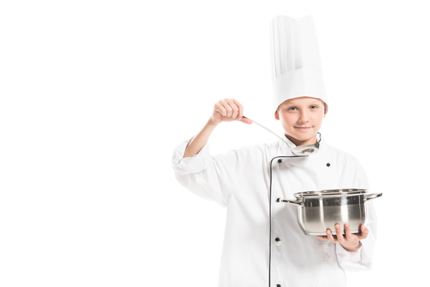 pre-adolescent boy in chef uniform with saucepan and ladle isolated on white - 写真・画像