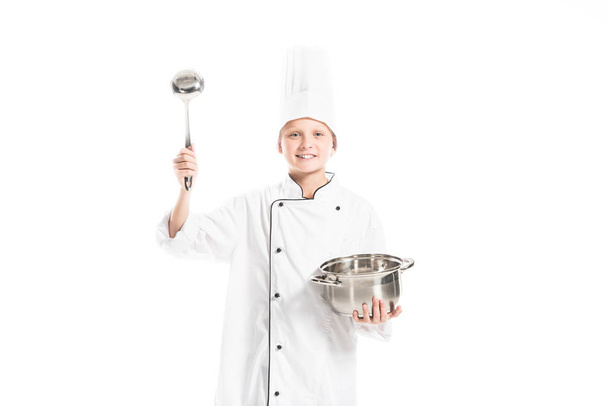 pre-adolescent boy in chef uniform with saucepan and ladle isolated on white - Φωτογραφία, εικόνα
