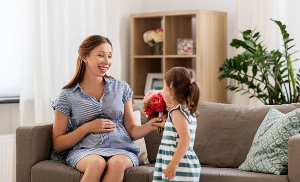girl giving flowers to her pregnant mother at home - Φωτογραφία, εικόνα