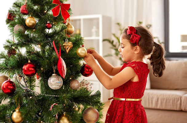 little girl decorating christmas tree at home - 写真・画像