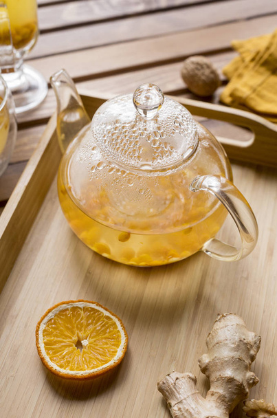 Glass teapot with sea buck thorn tea with ginger at wooden tray on wooden background - Foto, afbeelding