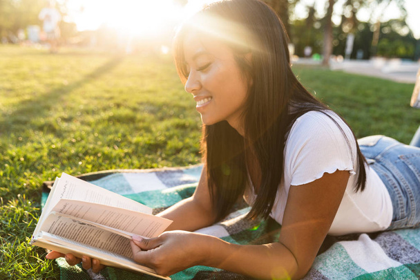 Image of happy smiling young asian girl outdoors in park reading book. - Fotó, kép