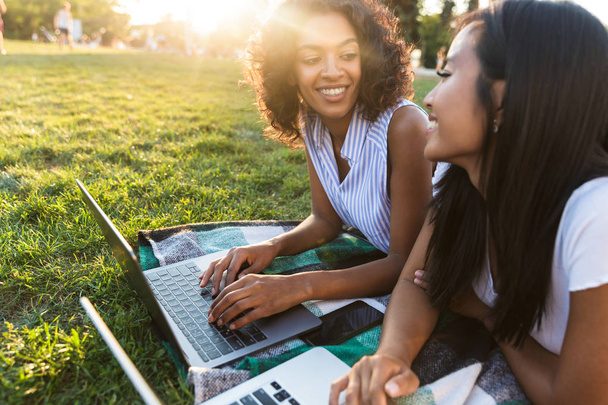 Image of happy smiling young friends girls outdoors in park using laptop computers. - Φωτογραφία, εικόνα