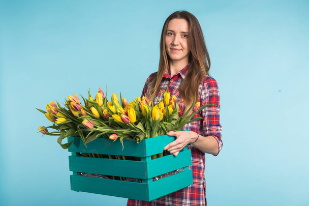 Joyeux caucasien jeune femme tenant boîte avec des tulipes sur fond bleu
 - Photo, image