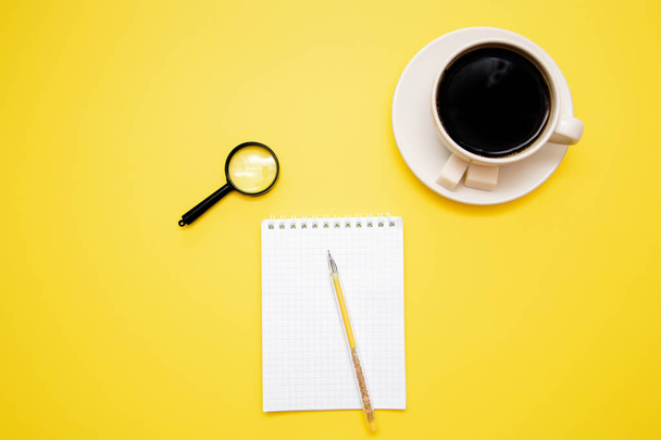 pen Notepad magnifier and coffee Cup on yellow background with copy space top view. - Foto, Imagem