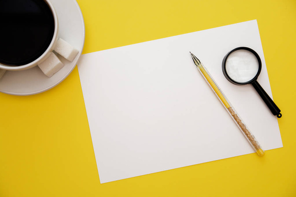 pen white paper magnifier and coffee Cup on yellow background with copy space top view. - Foto, immagini