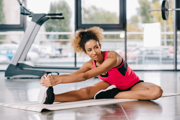 cheerful african american sportswoman stretching on fitness at gym - Zdjęcie, obraz