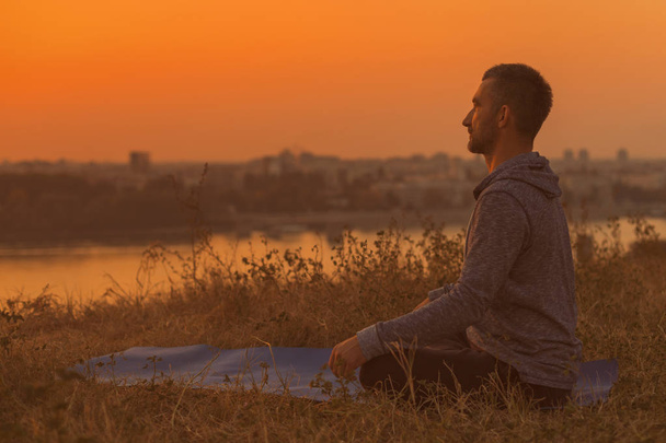 Man doing yoga on sunset with city view,Padmasana/Lotus position .Toned image. - 写真・画像