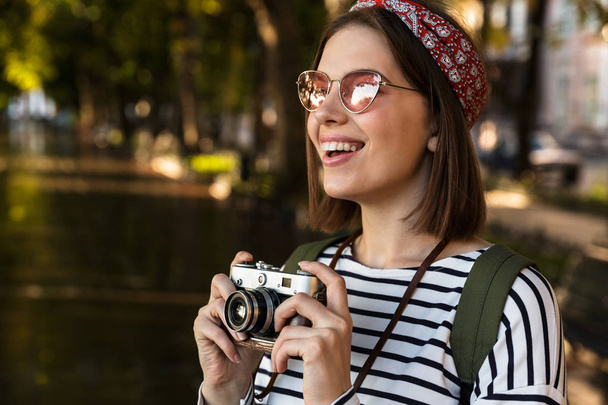 Image of excited young beautiful woman walking outdoors with camera. - Фото, изображение